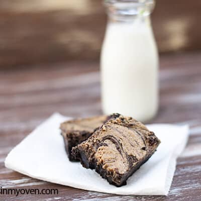 A peanut butter brownie on a napkin in front of a milk jar.