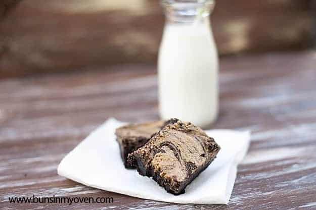 Two peanut butter brownies on a napkin in front of a milk jar.