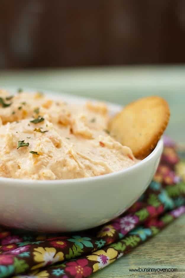 A close up of a bowl of pimento cheese dip with a ritz cracker in it.