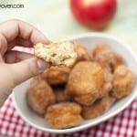 A woman holding an apple fritter with a bite taken out of it.