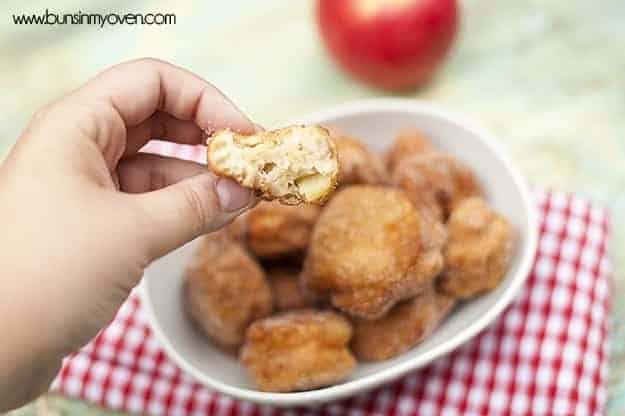 A person holding an apple fritter above a bowl of apple fritters