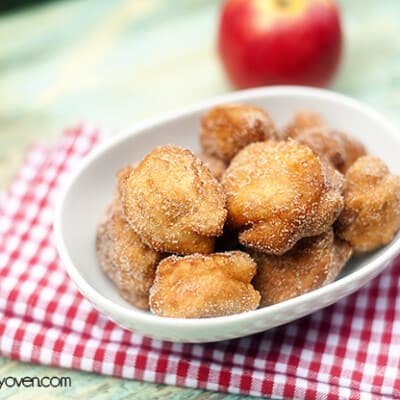 A close up of a bunch of apple fritters in an oval bowl.