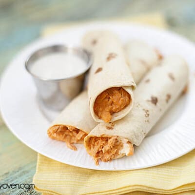 Some buffalo chicken taquitos on a white plate with ranch dressing.