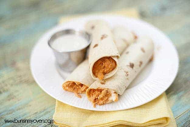 Some buffalo chicken taquitos on a white plate with ranch dressing.