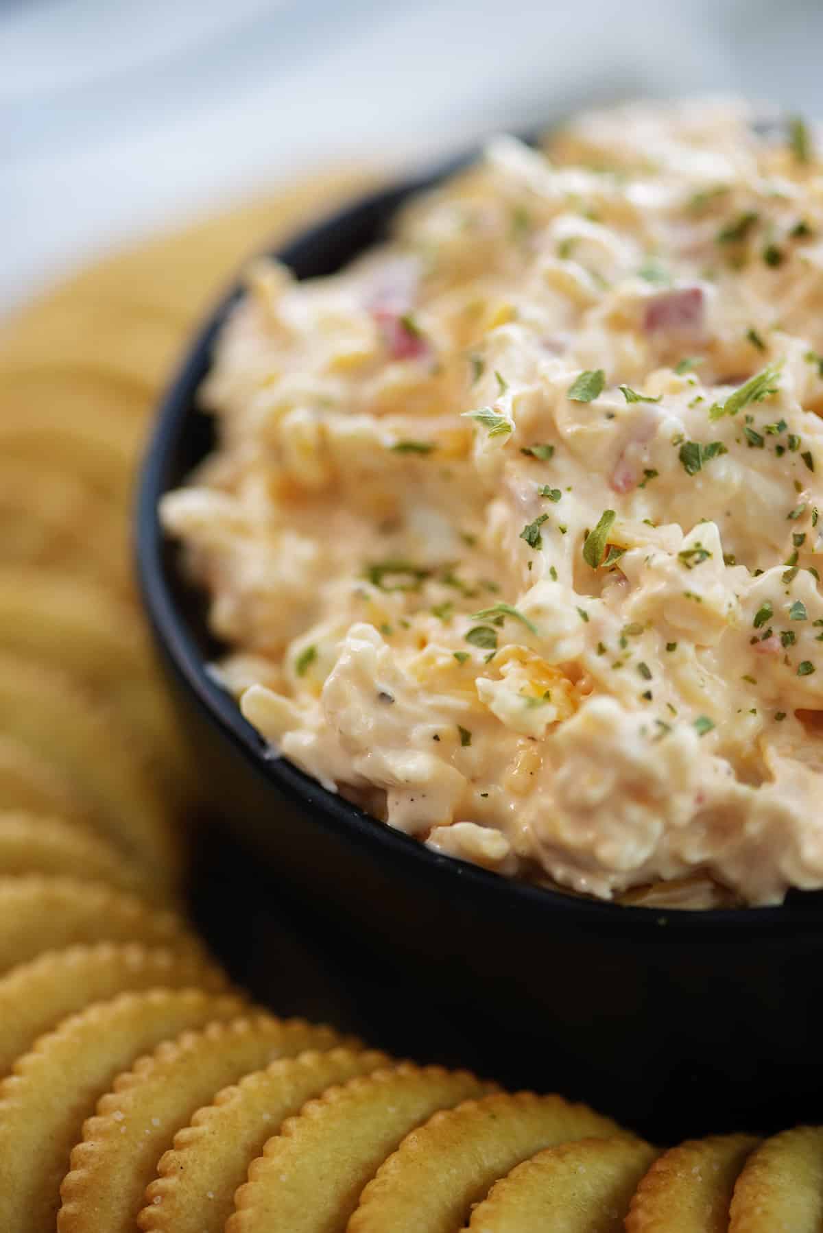 creamy pimento cheese in black bowl surrounded by crackers.