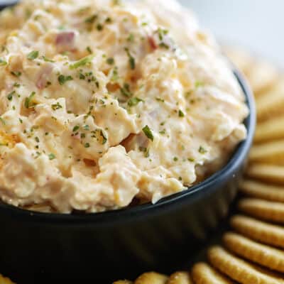 homemade pimento cheese dip in black bowl surrounded by ritz crackers.