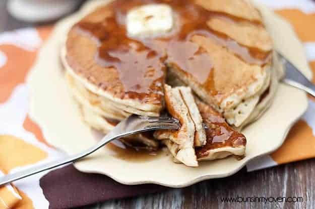 A plate of apple cider pancakes with a bite being cut out of it