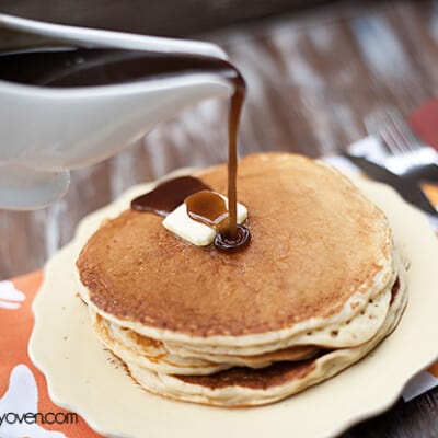 Cinnamon syrup being poured over a stack of pancakes