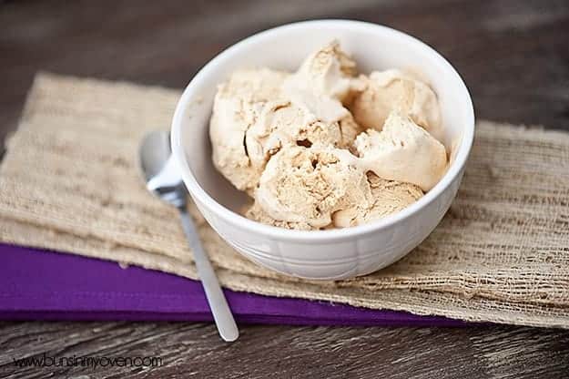 Pumpkin ice cream in a white bowl next to a spoon.