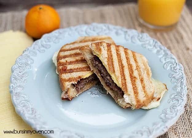 A sausage panini cut into triangle halves with an orange and orange juice in the background.