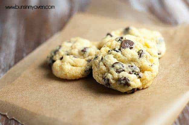 Three chocolate chip cookies on a piece of brown parchment paper.