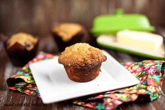 A blackberry muffin on a white plate on top of a cloth napkin.