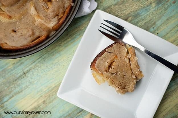 An overhead view of a cinnamon roll and fork on a white plate.