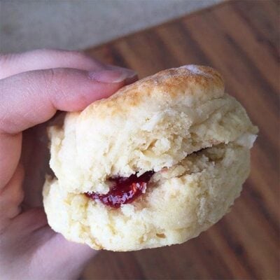 A woman holding up a biscuit with jelly in it.