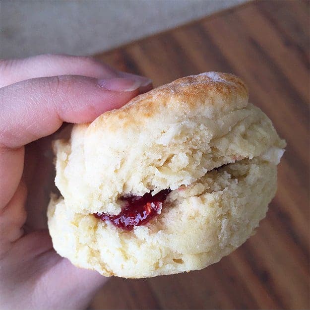 A woman holding up a biscuit with jelly in it.