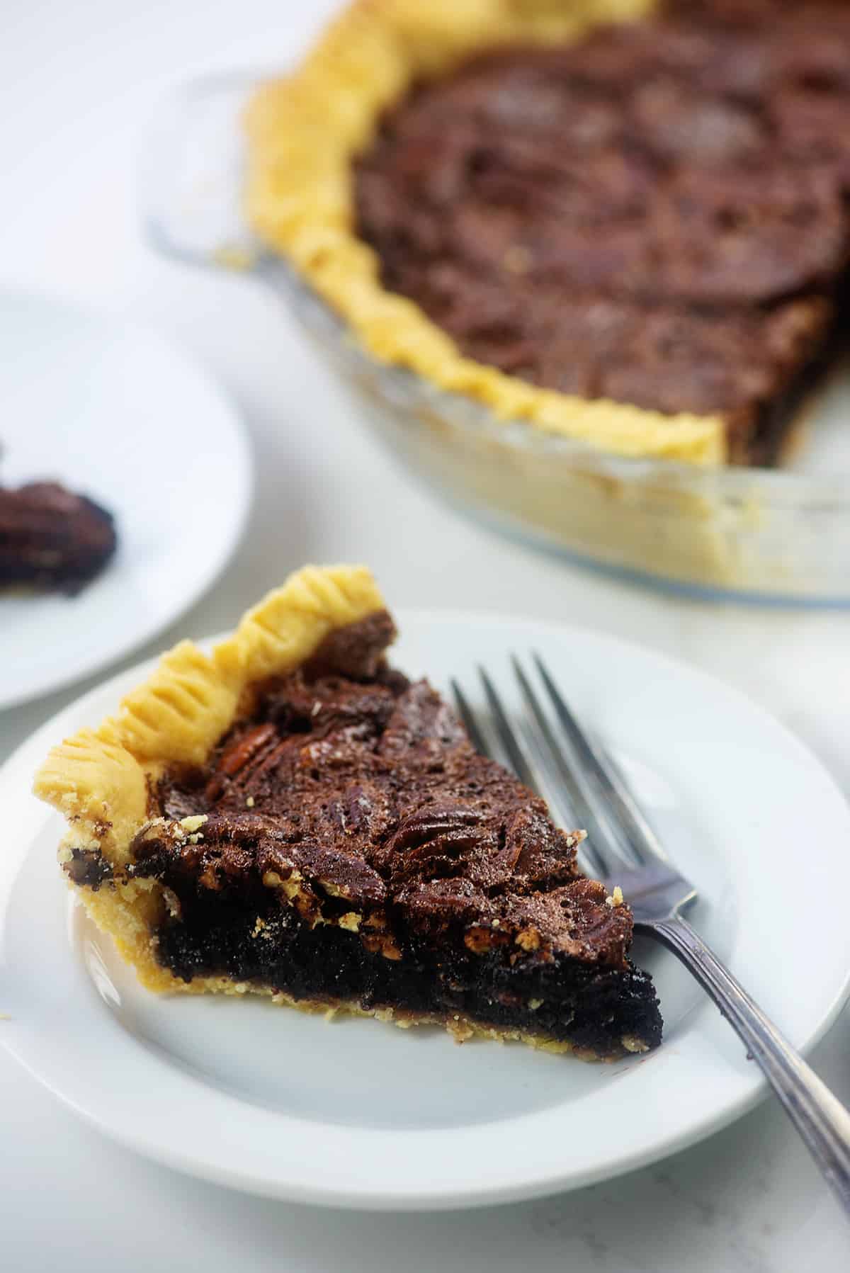 slice of chocolate pecan pie on white plate with fork.