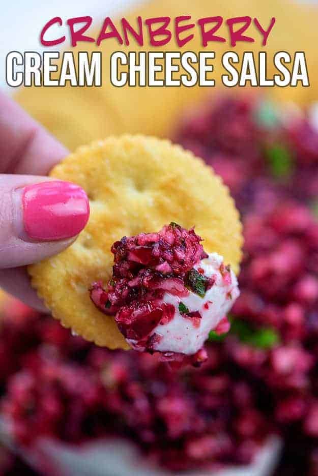 Woman holding a ritz cracker that has been dipped in cranberry salsa.