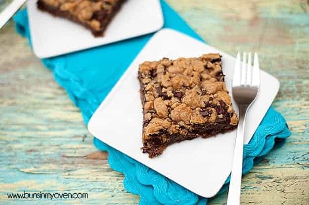 A piece chocolate chip cookie bar and a fork on a white plate.