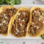 Carnitas tacos on white plate.