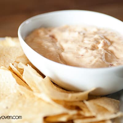 A white bowl of queso dip next to a bunch of tortilla chips on a table.