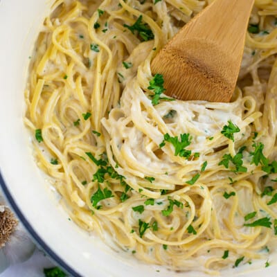 creamy garlic pasta in pot with wooden spoon.