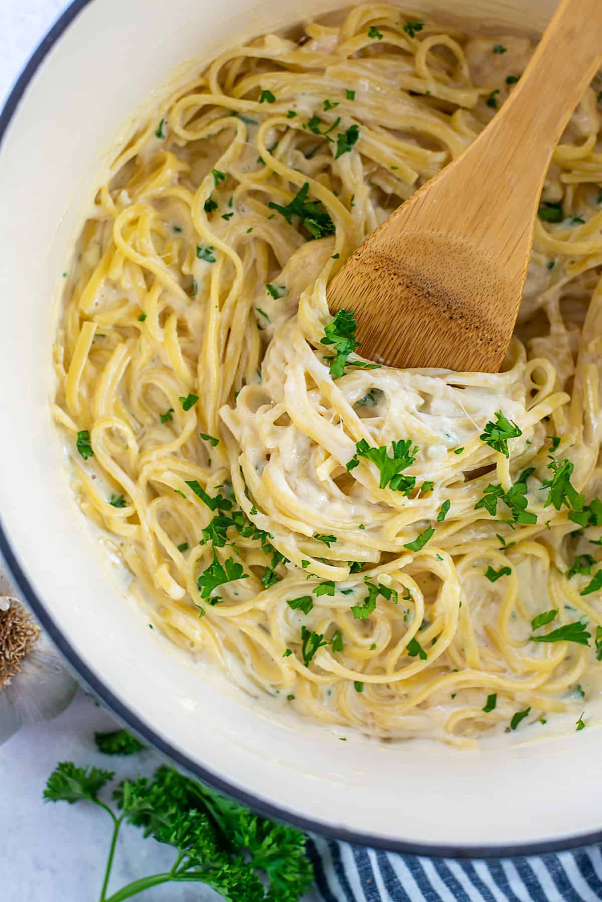 creamy garlic pasta in pot with wooden spoon.