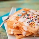 A stack of waffles with icing and sprinkles on top.