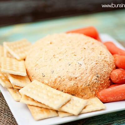 A cheeseball surrounded by crackers and carrots.