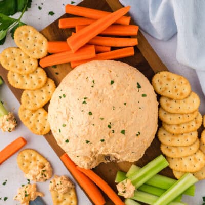 Buffalo chicken cheeseball on a wooden board with crackers, carrots, and celery.