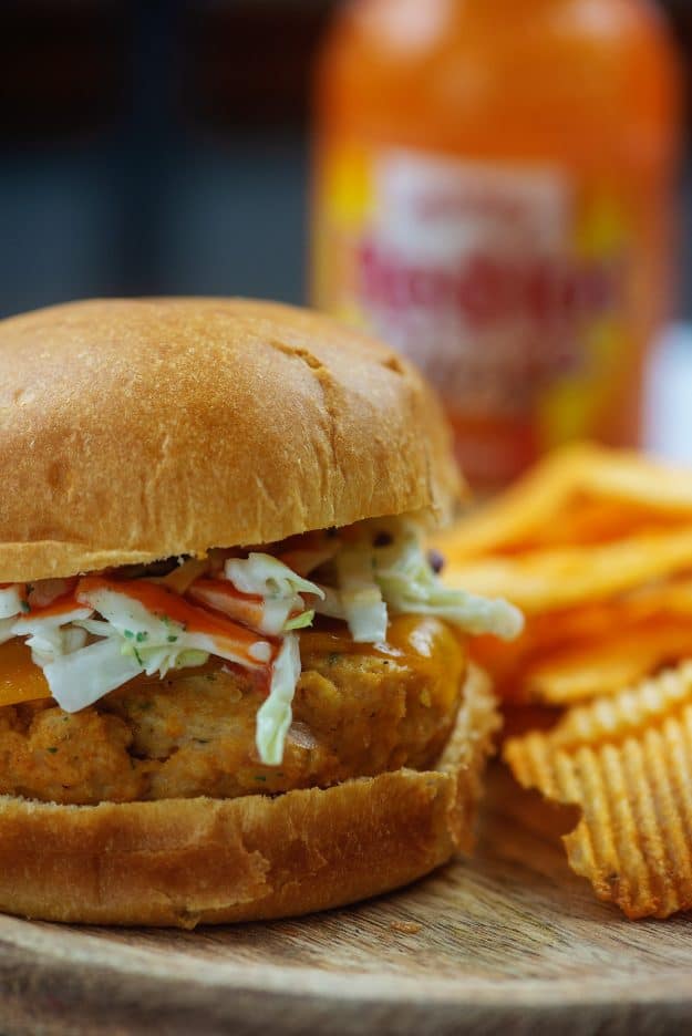 buffalo chicken burger with ranch coleslaw on cutting board by chips