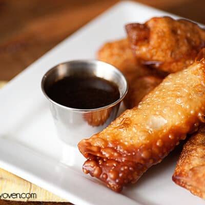Egg rolls and a small cup of dipping sauce on a plate.
