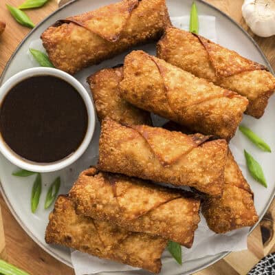 Egg rolls and a small cup of dipping sauce on a plate.