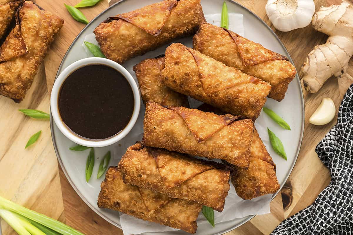 Egg rolls and a small cup of dipping sauce on a plate.