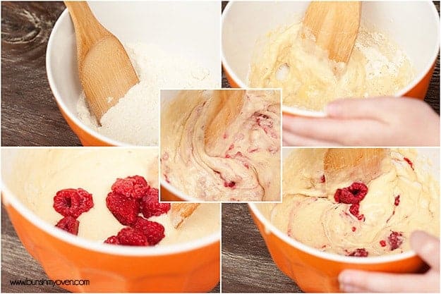 A wooden spoon in a bowl of dough with raspberries in it.