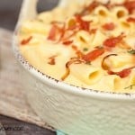 A white bowl of cheesy noodles topped with shoallots