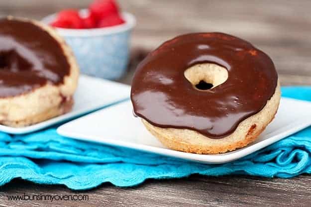 A close up of a chocolate frosted donut on a small square plate.