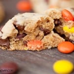A close up of a chocolate chip cookie split in half with some reeses pieces on it.