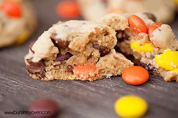 A close up of a chocolate chip cookie split in half with some reeses pieces on it.