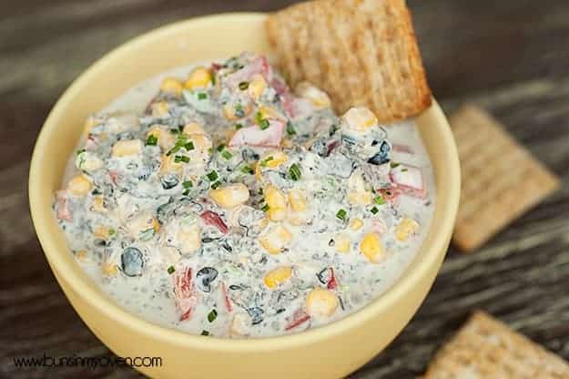 A bowl of dip with a wheat thin cracker in it.