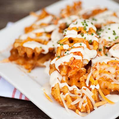 A closeup of buffalo chicken waffle fries on a Square white plate