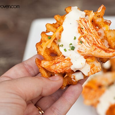 A person holding a waffle fry with ranch dressing on it