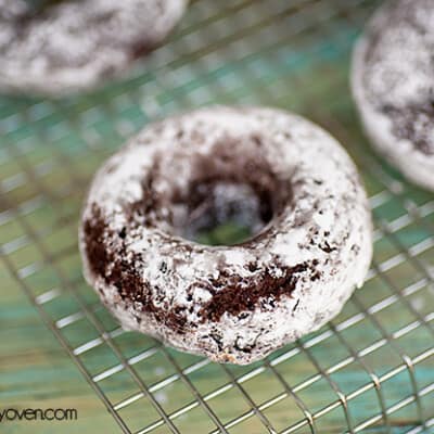 A couple chocolate doughnuts topped with powdered sugar on a wire cooling rack