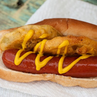 A closeup of a hot dog with fried green tomatoes and mustard on it