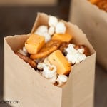 A close up of mini pretzels and popcorn in a paper bag.