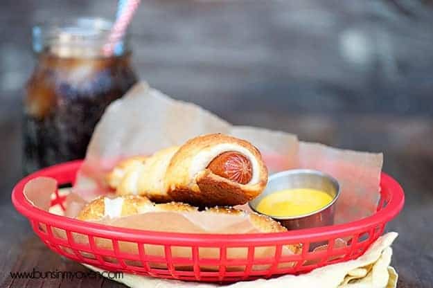 A closeup of two pretzel Dogs in a red appetizer dish 