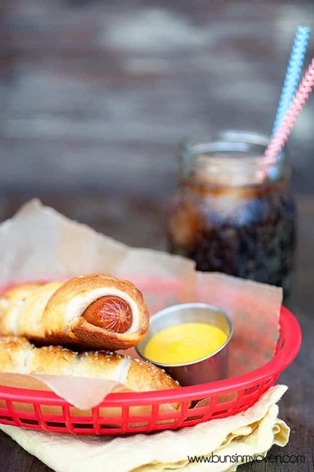 A pretzel wrapped hot dog in an appetizer serving dish and in front of a jar of ice tea 