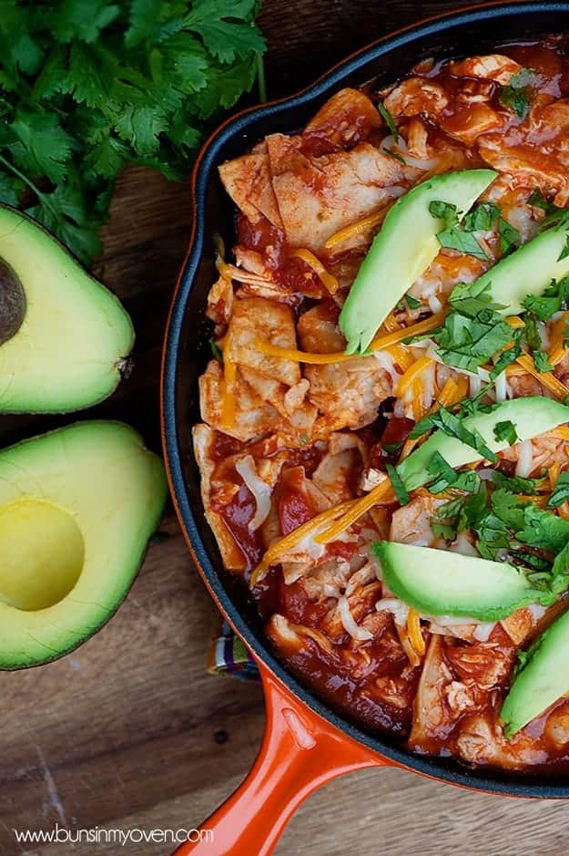 An overhead view of chicken enchilada in a skillet topped with avocado slices.