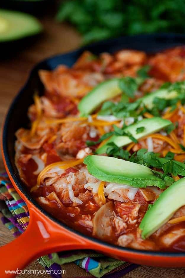 A cast iron skillet of chicken, avocado, and enchilada sauce.