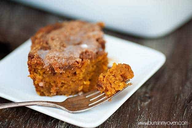 A fork with a bite of pumpkin coffee cake on it resting a white plate.