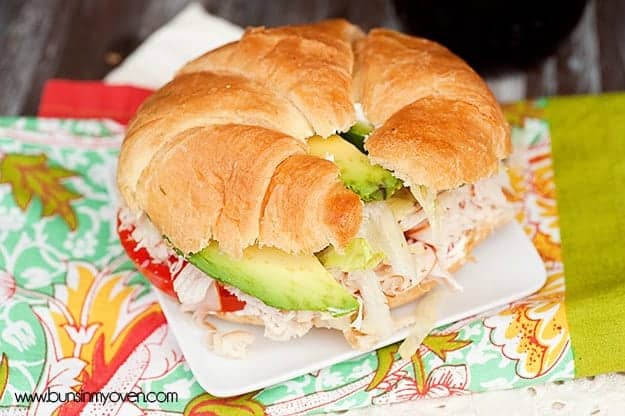 A close up of a turkey sandwich with a croissant bun on a white table.